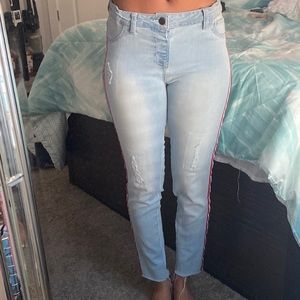 Denim jeans with small rips and pink, white, and navy blue stripes down the side